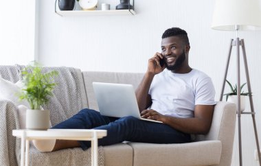 Bilgisayarda çalışan ve telefonla konuşan mutlu Afrikalı adam.