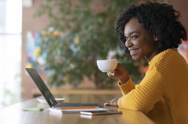 Laptopla çalışırken çay içen mutlu afro kız.