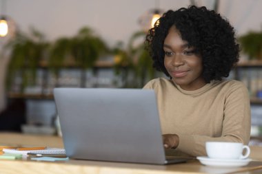 Genç siyah bayan çay içiyor ve dizüstü bilgisayar kullanıyor.