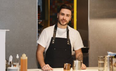Barista, kahve dükkanında kameraya gülümsüyor.