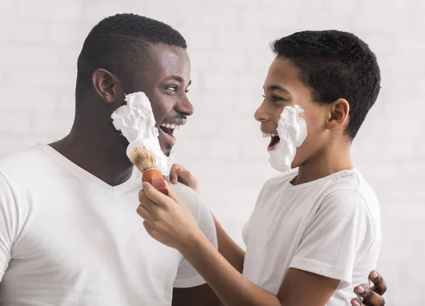 Afro father and son having fun while shaving in bathroom.