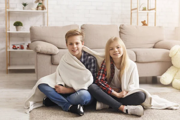 Roztomilý bratr a sestra přikryté dekou sedí na podlaze — Stock fotografie