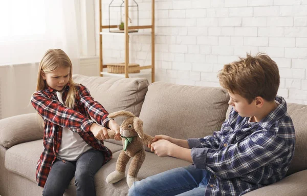 Gieriger Bruder und Schwester ziehen Spielzeug auseinander, das auf Sofa sitzt — Stockfoto