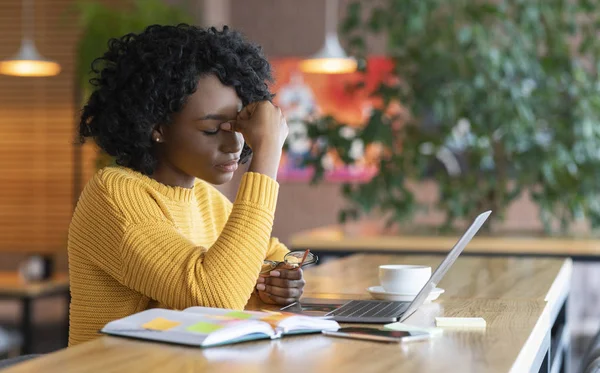 Cansado negro chica sentado en frente de la computadora portátil en la cafetería —  Fotos de Stock