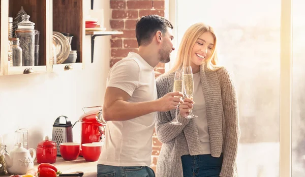 Pareja joven bebiendo champán y sonriendo en la cocina —  Fotos de Stock