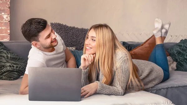 Jóvenes recién casados pareja acostada en la cama en casa y el uso de ordenador portátil —  Fotos de Stock