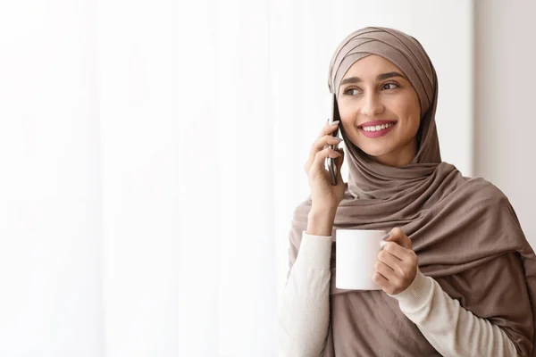Wanita Arab yang menarik Meminum Kopi dan Berbicara di Cellphone Dekat Jendela — Stok Foto