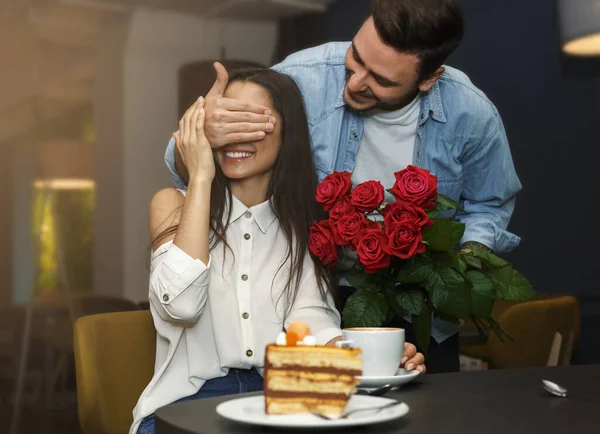 Homem amoroso cobrindo namoradas olhos dando seu buquê no café — Fotografia de Stock