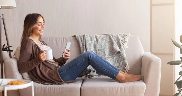 Young woman enjoying coffee and web surfing on smartphone