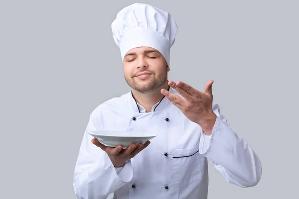 Chef Guy κρατώντας πιάτο μυρίζοντας Dish Posing πάνω από γκρι φόντο — Φωτογραφία Αρχείου