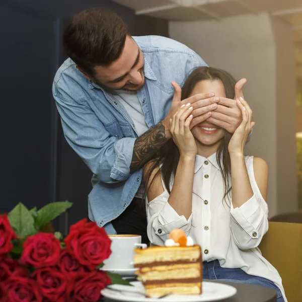 Uomo che copre fidanzate occhi congratularsi con lei con fiori in caffè — Foto Stock