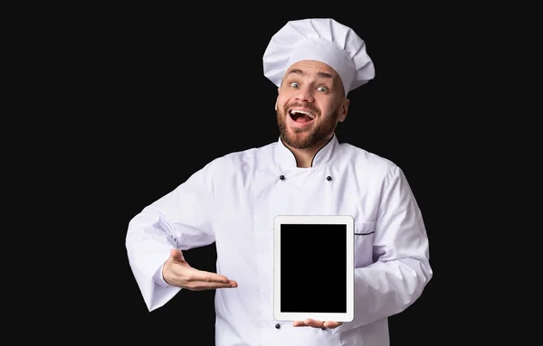 Волнующий парень-повар демонстрирует планшетный экран позируя в студии, макет — стоковое фото