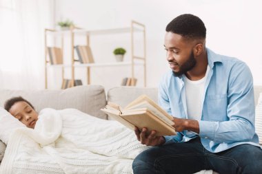 Afrikalı baba uyuyan kızı için kitap okuyor.