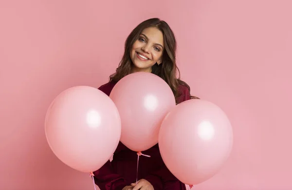 Chica positiva posando con tres globos rosados, de pie sobre fondo rosa — Foto de Stock