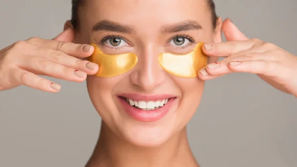 Lächelndes Mädchen, das goldenes Kollagen unter Augenklappen aufträgt — Stockfoto
