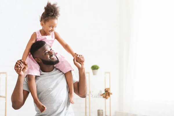 Söt afro flicka i rosa klänning sitter på pappor hals — Stockfoto