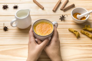 Baharatlı, ballı ve kükürtlü bir fincan latte tutan kadın eller.