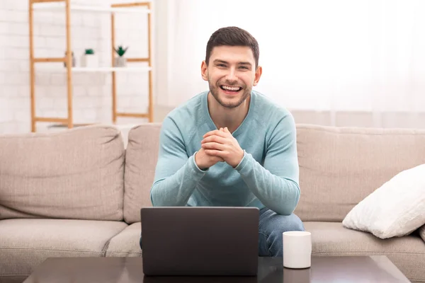 Chico en el ordenador portátil sonriendo sentado en el sofá en casa — Foto de Stock