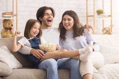 Küçük kız evde anne ve babasıyla komedi filmi izliyor.