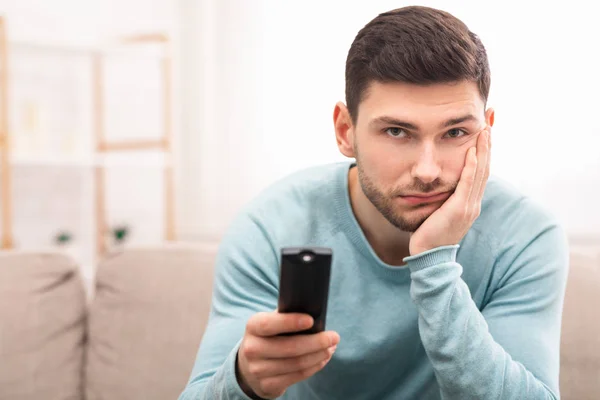 Jovem entediado assistindo TV sentado no sofá em casa — Fotografia de Stock