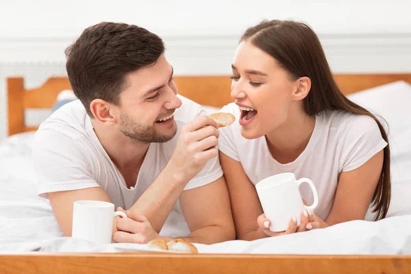 Pareja desayunando en la cama alimentándose mutuamente en el dormitorio — Foto de Stock