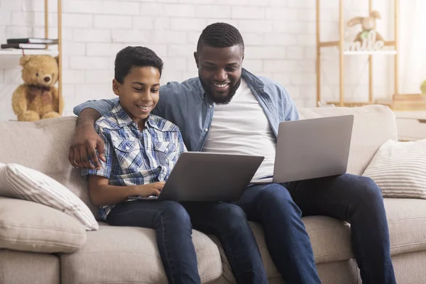 Alegre padre negro e hijo jugando videojuegos en línea en computadoras portátiles —  Fotos de Stock