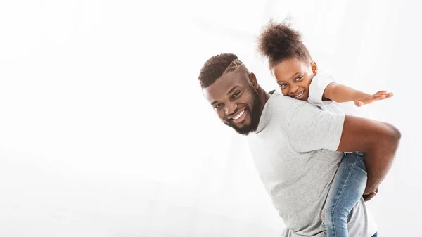 Щасливий чорний батько тримає свою маленьку дочку на спині — стокове фото