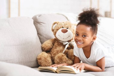 Tatlı afro bebek oyuncak ayıyla oynuyor, kitap okuyor.