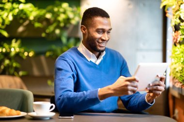 Kahve dükkanında oturan siyahi adam tabletini hazırlıyor.