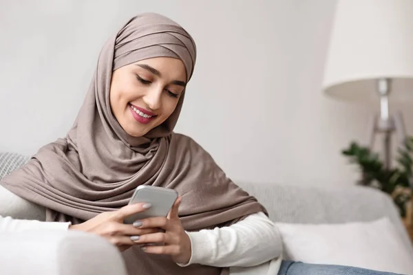 Gadis arab yang ceria dalam jilbab menghabiskan waktu dengan smartphone di rumah — Stok Foto