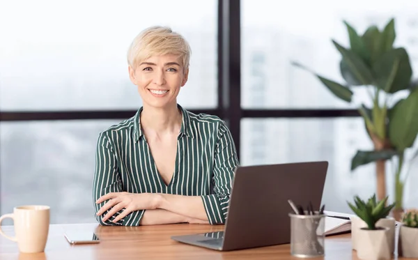 Επιτυχημένη επιχειρηματίας στο Laptop χαμογελώντας κάθεται στο σύγχρονο γραφείο — Φωτογραφία Αρχείου