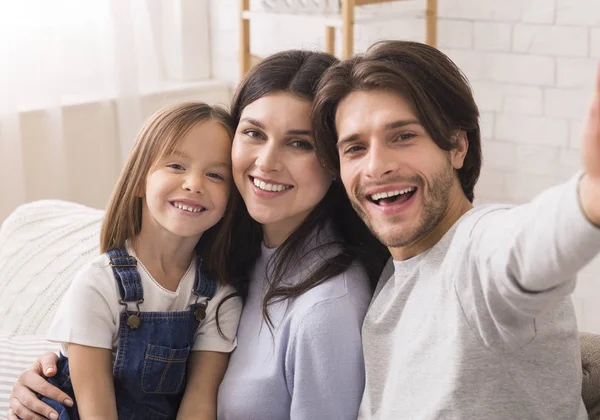 Šťastná rodina s roztomilou dceruškou pózující pro selfie doma — Stock fotografie