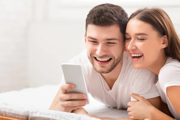 Щаслива пара використовуючи смс в ліжку в спальні — стокове фото