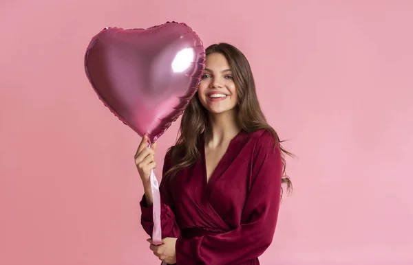 Красива молода жінка з повітряною кулею у формі серця на рожевому фоні — стокове фото