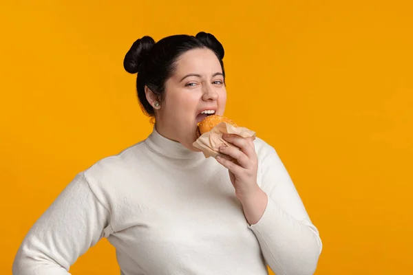 空腹プラスサイズの女の子とともに太りすぎ食べるおいしいバーガーとカメラを見て — ストック写真