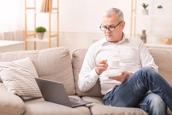 Hombre de edad avanzada utilizando ordenador portátil y tener café — Foto de Stock