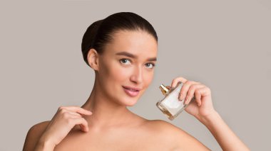 Pretty woman with perfume bottle looking at camera