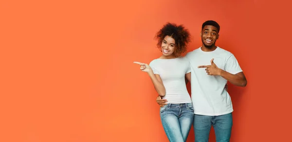 Afroamerykańska para wskazująca palcem na Copyspace, Pomarańczowe tło, Panorama — Zdjęcie stockowe