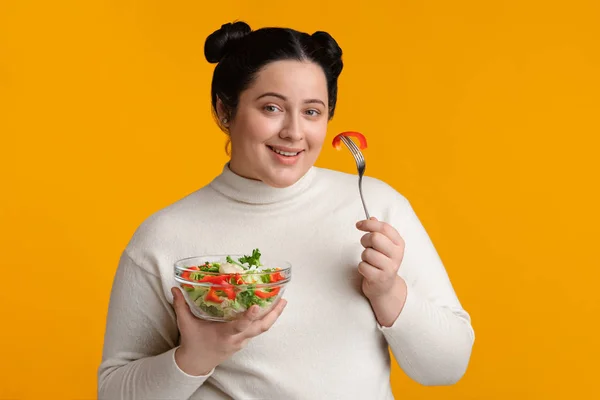 Happy Plumb meisje eten verse groenten salade, poseren over gele achtergrond — Stockfoto