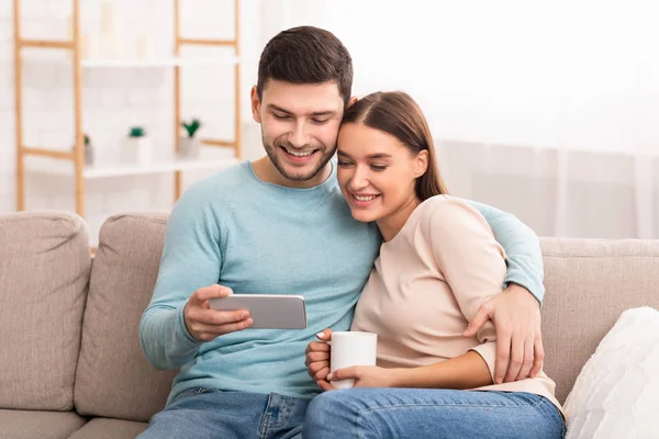 Casal feliz usando redes de smartphones sentado no sofá interior — Fotografia de Stock