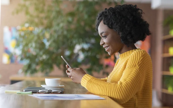 Hübsches Afro-Mädchen trinkt Kaffee und benutzt Smartphone — Stockfoto