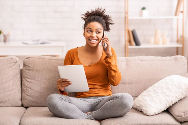 Black Woman Talking On Phone Using Tablet Sitting On Sofa — Stok fotoğraf