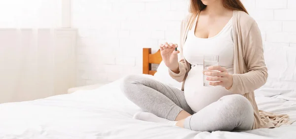 Pregnant woman taking vitamin pill, panorama, free space