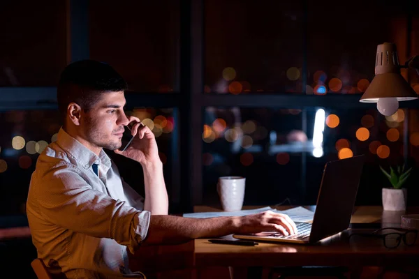 Uomo d'affari al computer portatile che parla al telefono che lavora durante la notte in ufficio — Foto Stock