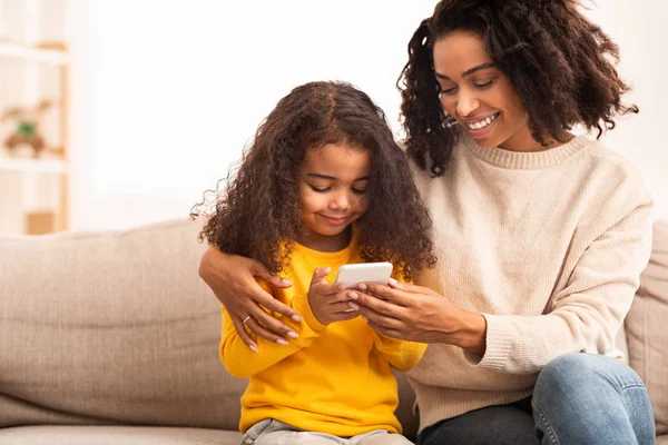 Afro madre e hija usando teléfono móvil sentado en sofá — Foto de Stock