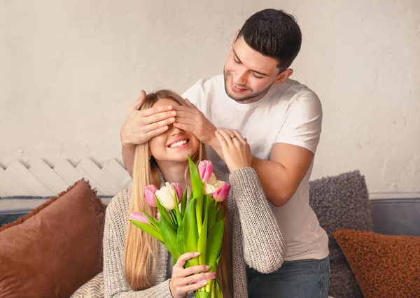 Handsome young man covering eyes of girlfriend and presenting her tulips — 图库照片