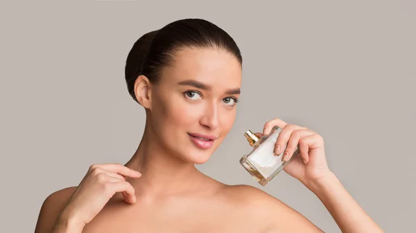 Hübsche Frau mit Parfümflasche blickt in die Kamera — Stockfoto