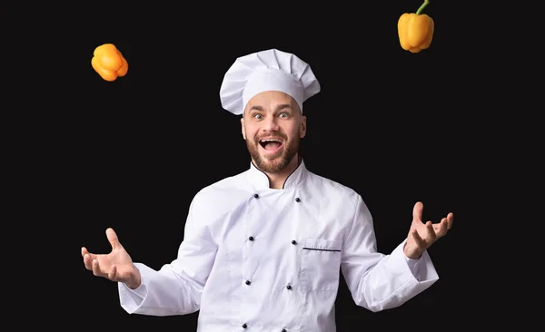 Eccitato chef ragazzo giocoleria cibo in piedi su sfondo nero — Foto Stock