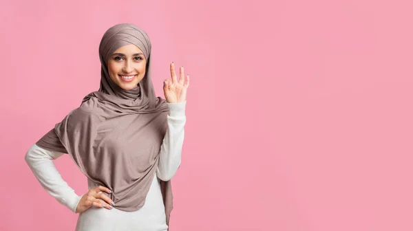 Smiling arabic girl in headscarf showing ok sign on pink background — 图库照片