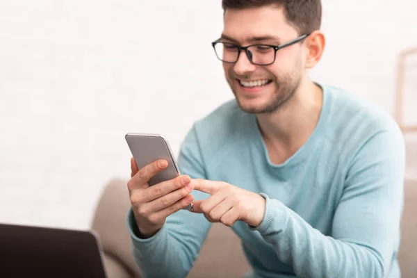 Joyful Guy Using Smartphone Texting Sitting On Couch At Home — ストック写真